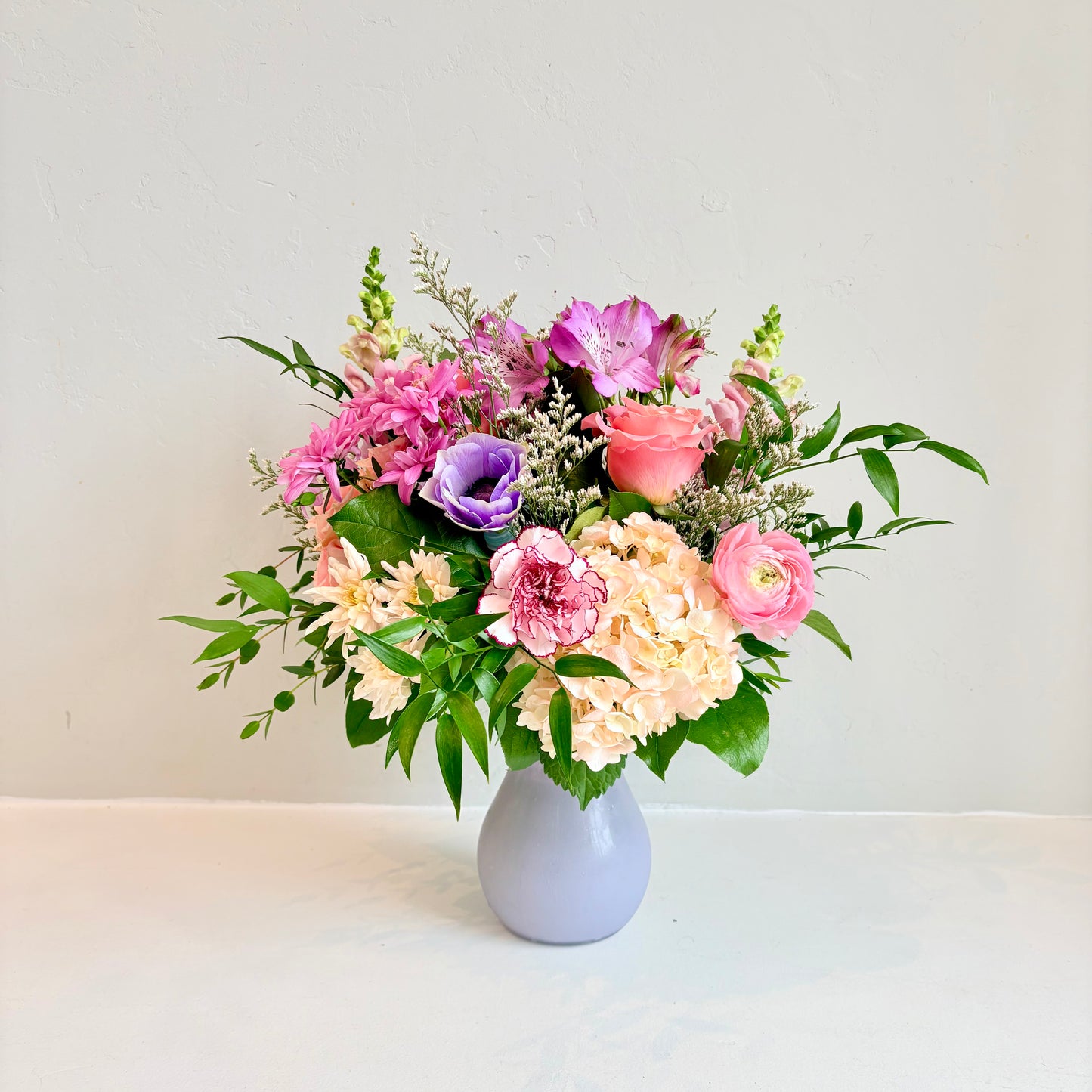 This arrangement is designed in a tiffany style vase in a mix of soft pinks, purples and whites and pops of brighter colours. It includes a mix of textures, greenery and is similar to our garden style.