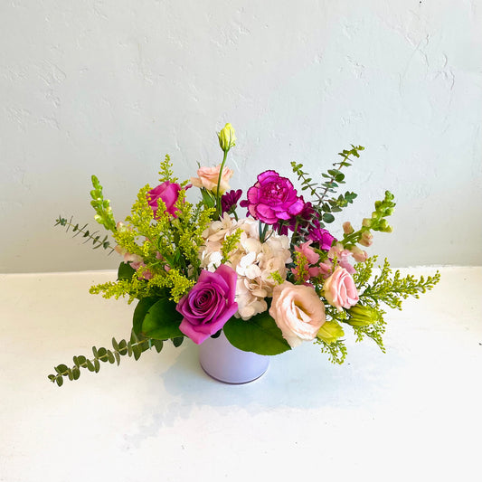 A small pink vase arrangement using assorted seasonal  flowers in shades of white, pink, cream, lavender and purples. Designed in a whimsical, garden style. 
